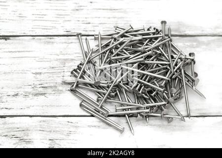 Mucchio di chiodi metallici argentati su sfondo bianco in legno Foto Stock