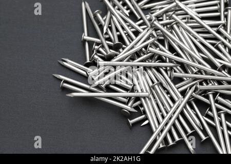 Mucchio di chiodi metallici argentati su sfondo nero Foto Stock