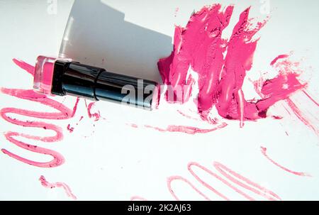 Un tubo di rossetto su macchie di rossetto rosso, isolato su sfondo bianco. Texture e ombra cremose per il trucco. Vista dall'alto Foto Stock