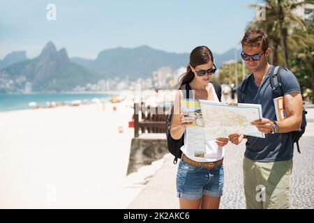 Perdersi in paradiso non è così male. Scatto di una giovane coppia che guarda una mappa mentre si trova su una spiaggia. Foto Stock