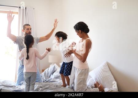 Il divertimento non si ferma mai a casa nostra. Scatto di una bella giovane famiglia di quattro divertirsi e trascorrere il tempo insieme nella loro camera da letto a casa. Foto Stock