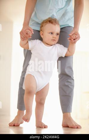 Prendendo i suoi primi passi.... Immagine ritagliata delle gambe di un bambino che cammina con un genitore che sostiene da dietro. Foto Stock