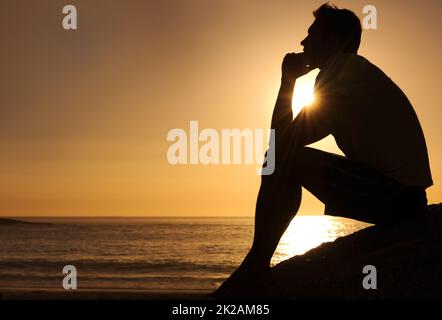 Ricerca di risposte lifes. Silhouette di un uomo pensieroso seduto accanto all'oceano - copyspace. Foto Stock