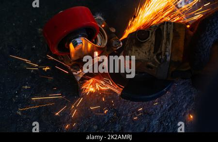 Operatore industriale che utilizza una smerigliatrice angolare per tagliare metalli. Operatore che lavora con smerigliatrice angolare e ha scintille arancioni. Utensile per tagliare e smerigliare l'acciaio. Sicurezza sul luogo di lavoro industriale. Industria metallurgica. Foto Stock