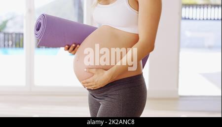 Mi hanno detto che lo yoga era buono per il bambino. Scatto corto di una giovane donna incinta irriconoscibile che porta un tappeto yoga. Foto Stock