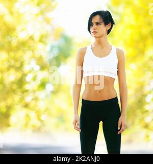 Determinato per riuscire al suo workout. Una giovane donna in forma in piedi all'aperto e guardando lontano. Foto Stock
