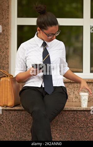 Shes sempre connessi. Una bella giovane donna seduta con il suo tablet digitale e raggiungere per il suo caffè. Foto Stock