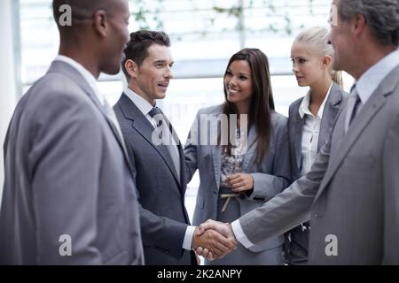 Salire sulla scala aziendale. Un gruppo diversificato di uomini d'affari che cercano come un collega e il loro capo scuote le mani. Foto Stock