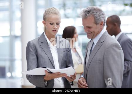 Cercando il suo consiglio rispettato. Una donna d'affari graziosa che presenta un raccoglitore ad un esecutivo superiore impressionato. Foto Stock