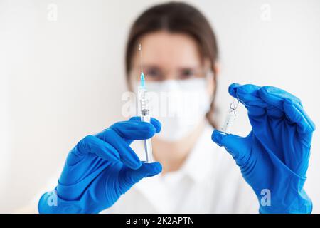 Un giovane medico con una siringa e un vaccino in mano. Il medico al chiuso fa la vaccinazione. Una donna in un ufficio medico. Vaccinazione contro l'influenza e i virus. Foto Stock