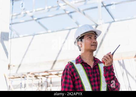 Ingegnere asiatico caposquadra architetto lavoratore uomo che lavora a costruire cantiere sito parlando con la radio Foto Stock