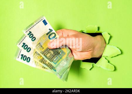 Uomo d'affari che infrange attraverso il libro verde con mazzo di fatture dell'euro in mano Foto Stock