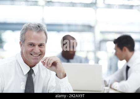 HES un datore di lavoro ben equilibrato. Ritratto di un uomo d'affari maturo sorridente mentre si siede di fronte a due colleghi più giovani. Foto Stock