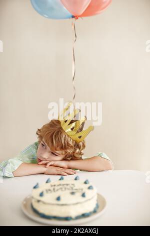 Wheres il divertimento. Scatto di un ragazzino carino che sembra infelice mentre si siede a un tavolo con la sua torta di compleanno. Foto Stock