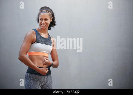 Theres sempre tempo di flessione. Scatto corto di una giovane donna sportiva che flette le braccia davanti ad un muro grigio. Foto Stock