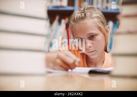 Duro al lavoro. Una ragazza giovane carina che fa il lavoro di scuola mentre circondato da libri alla biblioteca. Foto Stock