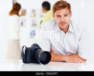 Fotografo seduto al tavolo. Ritratto di fotografo seduto a tavola con la gente che guarda le immagini sullo sfondo. Foto Stock