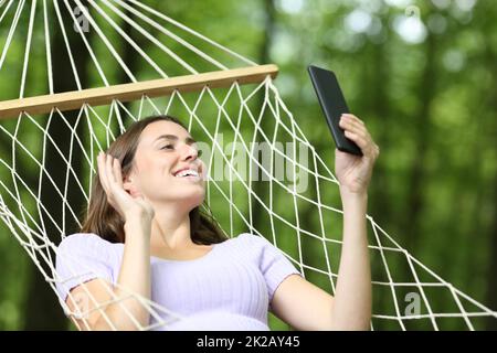 Donna felice che ha videocall al telefono su amaca Foto Stock