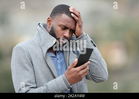 Uomo preoccupato con la pelle nera che controlla il telefono in inverno Foto Stock