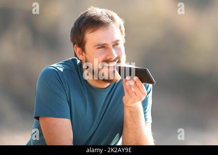 Uomo felice che usa il riconoscimento vocale sul cellulare all'aperto Foto Stock