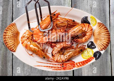 Primo piano di gamberi o gamberetti freschi grigliati su un piatto colorato di frutti di mare su un tavolo rustico con tela a plaid. Concetto di cibo sano. BARBECUE. Pesce sfondo. Pubblicità spaziale. Foto Stock