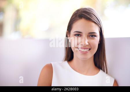 Il suo sorriso illumina la stanza. Scatto corto di una giovane donna appoggiata contro un muro. Foto Stock