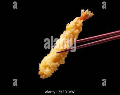 Tempura di gamberetti sollevata con bacchette contro uno sfondo nero. Foto Stock