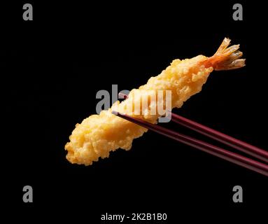Tempura di gamberetti sollevata con bacchette contro uno sfondo nero. Foto Stock