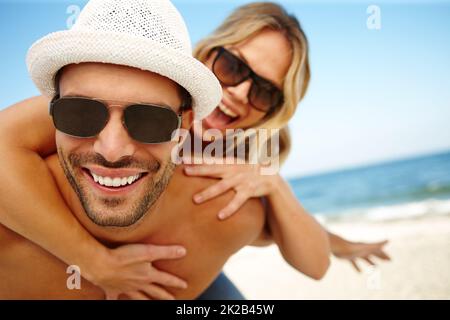 La migliore vacanza MAI. Scatto di un giovane sorridente che dà alla sua ragazza ridente un piggyback su una spiaggia soleggiata. Foto Stock