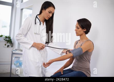 Sensazione di una leggera pressione sulle prestazioni. Shot di una giovane donna che ottiene la sua pressione sanguigna testato da un medico. Foto Stock