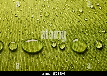 Vista dall'alto del tessuto verde con gocce d'acqua in primo piano su tessuto bagnato rivestito con membrana impermeabile in ambienti luminosi Foto Stock