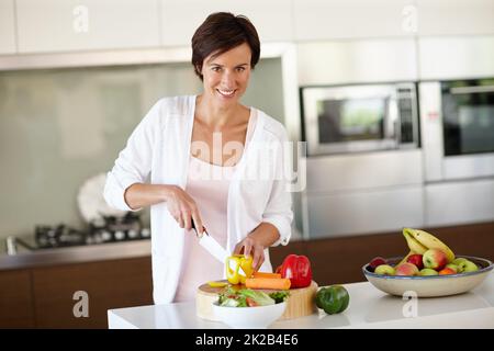 Creare un piatto delizioso da zero. Ritratto di una donna attraente tritare verdure al banco della cucina. Foto Stock