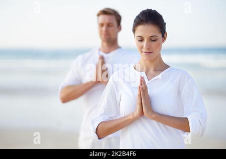 Yoga sul mare. Una giovane coppia che pratica yoga sulla spiaggia. Foto Stock