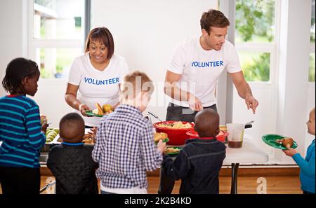 La generosità continua a dare. Shot di volontari che servono cibo a un gruppo di bambini piccoli. Foto Stock