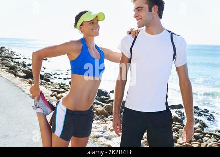 Limbering in su. Una giovane donna attraente appoggiata sul suo ragazzo mentre allunga i suoi quads. Foto Stock