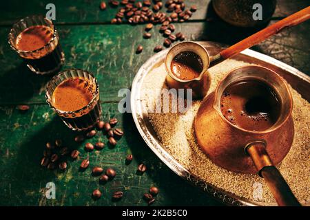 Alto angolo di caffè orientale caldo appena preparato in cezves e bicchieri posti su un tavolo verde shabby in cucina leggera Foto Stock