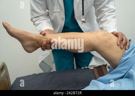 Medico asiatico fisioterapista esame, massaggio e trattamento ginocchio e gamba di paziente anziano in ospedale medico ambulatorio ortopedist infermiere. Foto Stock