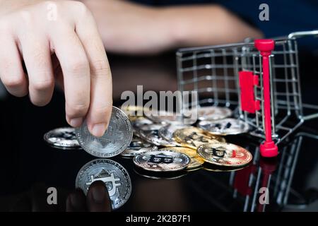 Donna che tiene alcuni pezzi di gettone Bitcoin d'oro nel carrello della spesa Foto Stock