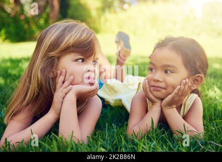 Amicizia infantile. Shot di due adorabili bambine che giacciono l'una accanto all'altra sull'erba. Foto Stock