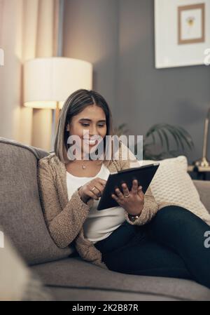 Trasformando il suo tablet in un mini tv. Scatto di una giovane donna con un tablet digitale sul divano di casa. Foto Stock