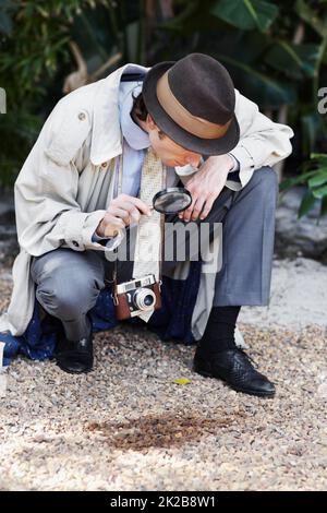 HES ha ottenuto un occhio investigativo acuto. Curioso investigatore privato guardando attraverso una lente di ingrandimento al suolo per gli indizi. Foto Stock