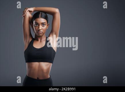 Iniziamo questo allenamento con alcuni tratti potenti. Ritratto da studio di una giovane donna sportiva che allunga le braccia su uno sfondo grigio. Foto Stock