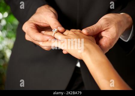 Pedging il loro amore. Vista spezzata di uno sposo che scivola un anello sul suo dito sposa. Foto Stock