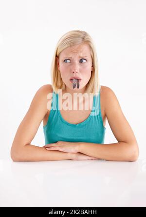 Non mangiatelo se devo. Una giovane donna che tira un volto con un pesce in bocca. Foto Stock