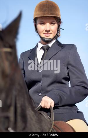 Cavalca come il vento. Ritratto ad angolo basso di una giovane donna seduta sul suo cavallo. Foto Stock