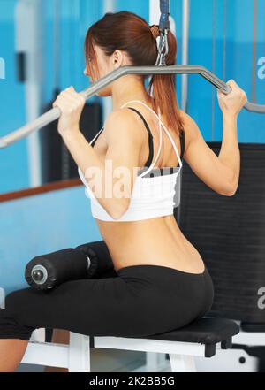 Tirando la sua strada per tonificare i muscoli. Vista posteriore di una giovane donna attraente che lavora le spalle in palestra. Foto Stock