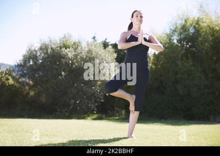 Ricerca di pace nel giardino. Scatto a tutta lunghezza di una donna attraente che pratica yoga. Foto Stock