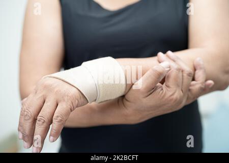 Donna asiatica di mezza età usa bendaggio elastico per curare la sindrome di De Quervain a portata di mano e dito in ufficio. Foto Stock