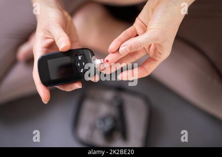 Analisi degli zuccheri nel sangue a casa. Donna che controlla il livello di zucchero nel sangue con glucometro e striscia di prova a casa. Diabetici che controllano i livelli di zucchero nel sangue. Foto Stock