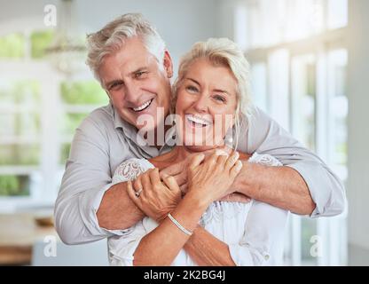 Amore, coppia e pensione con un anziano uomo e donna che guarda felice e abbracciando nella loro casa insieme. Sorriso, romanticismo e rapporto con un Foto Stock